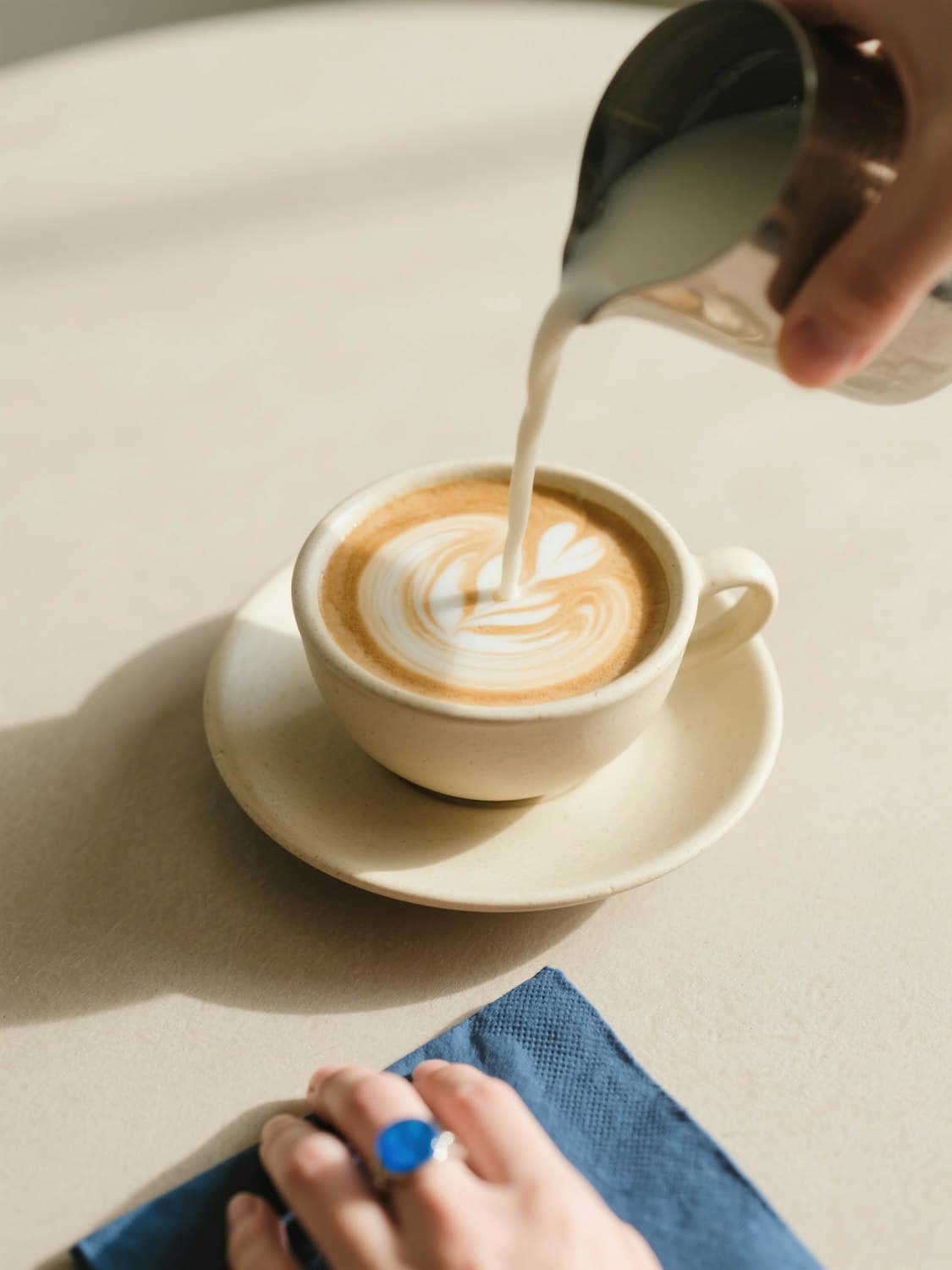 Barista pouring latte art into a cream ceramic cup