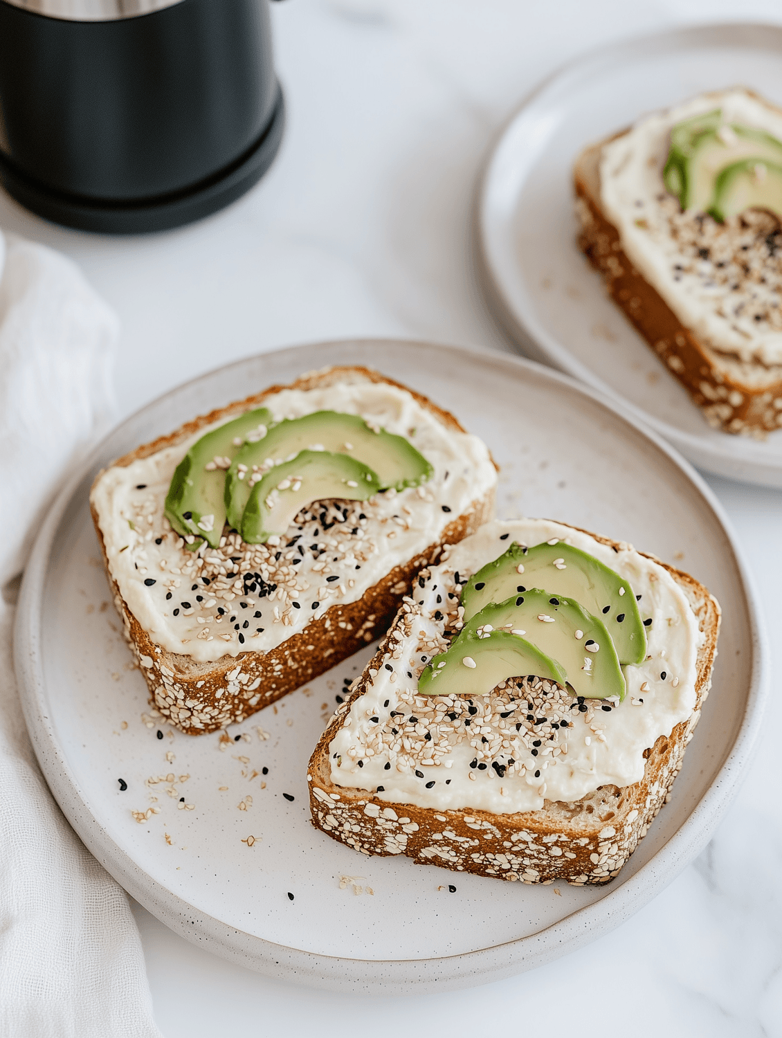 Two slices of seeded toast topped with whipped feta, sliced avocado and sesame seeds
